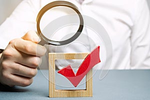 A man examines a red check mark through a magnifying glass. Assessing the transparency of the legitimacy of an election