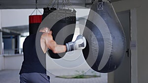 The man executes strong blows in the boxing bag, outdoors
