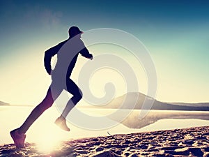 Man exercising on beach. Silhouette of active man exercising and stretching at lake