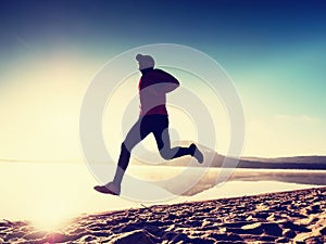 Man exercising on beach. Silhouette of active man exercising and stretching at lake