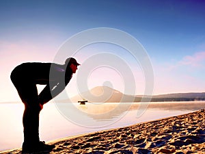 Man exercising on beach. Silhouette of active man exercising and stretching at lake