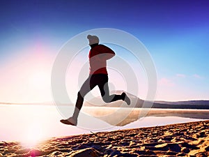 Man exercising on beach. Silhouette of active man exercising and stretching at lake