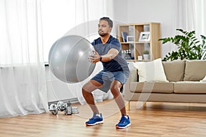 Man exercising and doing squats with ball at home