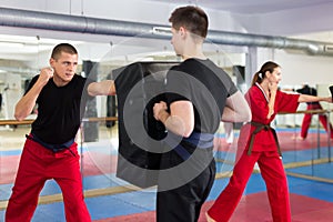 Man exercising jabs on punching pad during group karate training