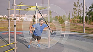 Man exercising outside in sunny park. Great TRX workout and exercising outdoors