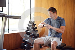 Man Exercising Sitting On Weight Bench In Home Gym Checking Smart Watch