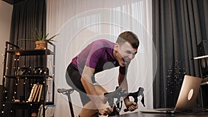 Man is exercising on stationary bicycle at home. Cyclist is spinning pedals on indoor smart bike trainer. Male athlete is doing wo