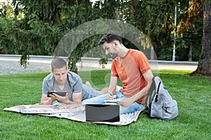 Man explaining something to her friend in laptop. students studying at park and smiling. Group of students leusure, talking outdoo photo