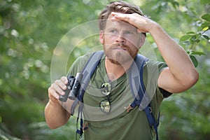 man explorer in forest scanning horizon with binoculars