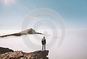 Man explorer standing alone on cliff edge mountain over clouds