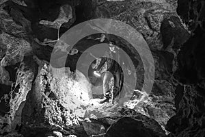 Man exploring huge cave. Adventure travellers dressed cowboy hat and backpack, leather jacket. black and white, tourist route.