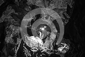 Man exploring huge cave. Adventure travellers dressed cowboy hat and backpack, leather jacket. black and white, tourist route.