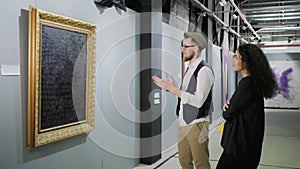 Man is expressing his opinion about picture in art gallery, woman is listening