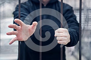 Man extends his hand for help from cage. Closeup on hands of man sitting in jail, prisoner concept. Hope to be free