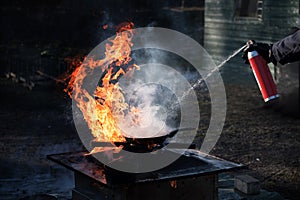 Man extinguishing the fire on an iron pan with foam from a spray