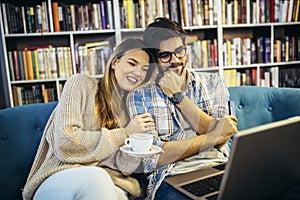 Man in eyeglasses and charming woman using laptop resting at cafe with cup of coffee