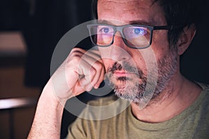 Man with eyeglasses looking at computer screen in dark room, reflection of display content on his eyewear