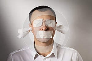 A man with eyes, mouth and ears sealed with painting tape. A concept on the topic of fear of telling the truth