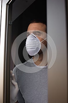 Man with face mask and gloves looking out the window.