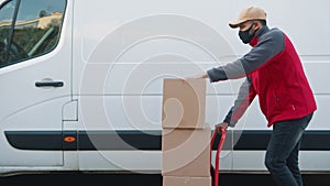 Man with face mask pushing cardboard boxes on the troley. Delivery of parcels during covid19 outbreak