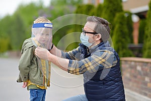 Man in facemask putting face shield on child on street or park. Safety during COVID-19 outbreak. Lifting virus lockdown. Social photo