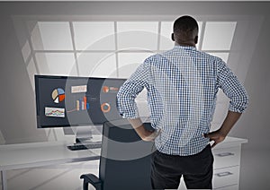 Man facing away looking out office window while data is on computer screen