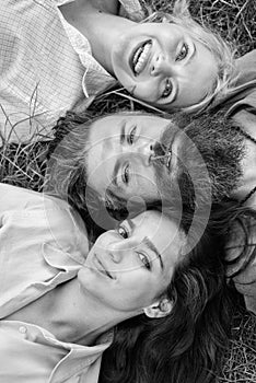Man fall in love both women. Happy threesome. Man bearded hipster lay on grass with two girls blonde and brunette