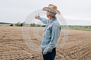 Man farmer agronomist in jeans and shirt stands back in field after haymaking  with tablet looking into the distance. Rural