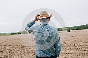 Man farmer agronomist in jeans and shirt stands back in field after haymaking  with tablet looking into the distance. Rural