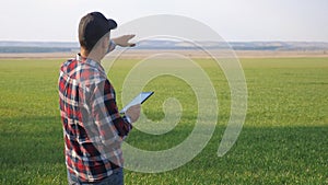 man farmer red neck with a digital tablet walks on green field. eco smart farming agriculture concept. male lifestyle