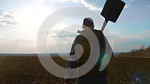 Man farmer silhouette red neck holding a shovel in his hand walking across the field a pile of dirt soil. Eco smart