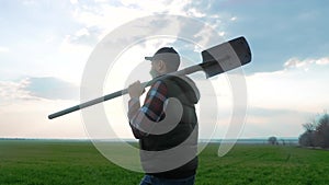 Man farmer a silhouette red neck holding shovel in his hand walking across green field a pile of dirt soil. Eco smart