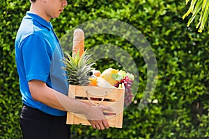 Man farmer wears delivery uniform he holding full fresh vegetables and fruits in crate wood box