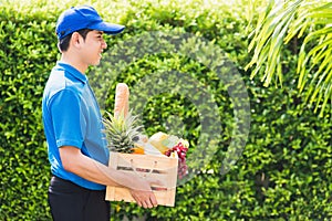 Man farmer wears delivery uniform he holding full fresh vegetables and fruits in crate wood box