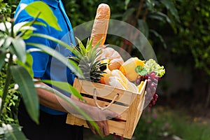 Man farmer wears delivery uniform he holding full fresh vegetables and fruits in crate wood box