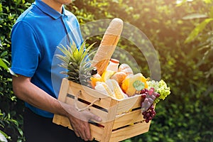 Man farmer wears delivery uniform he holding full fresh vegetables and fruits in crate wood box