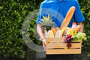 Man farmer wears delivery uniform he holding full fresh vegetables and fruits in crate wood box