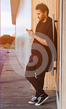 A man in a fashionable black outfit posing at the sunset of a warm summer day in trainers. Streetstyle.