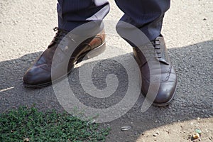 A man in fashionable and expensive genuine leather shoes stands on the border of asphalt and country soil