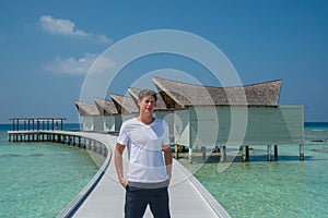 Man in fashionable white t-shirt and black shorts at over water villas at tropical island luxury resort