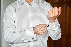 man fastens cufflinks on the sleeve of a white shirt