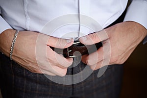 A man fastens a leather belt on his trousers, close-up. Young modern businessman,groom. Business style clothing concept.