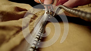 A man fastens a metal zipper on a beige jacket in macro. Extreme close up zipper with hand fastens clothing, while