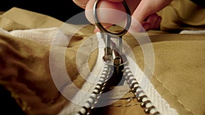 A man fastens a metal zipper on a beige jacket in macro. Extreme close up zipper with hand fastens clothing, while