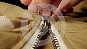 A man fastens a metal zipper on a beige jacket in macro. Extreme close up zipper with hand fastens clothing, while