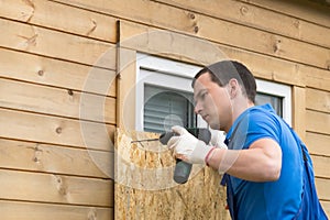 A man fastens a plywood sheet to protect the windows from natural disasters