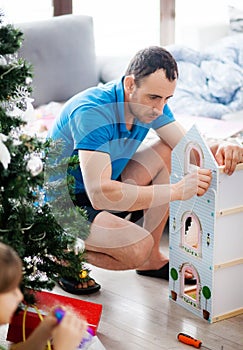 Man father collects for his daughter a dollhouse wooden house Christmas