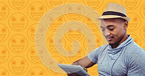 Man in fedora with tablet against yellow emoji pattern