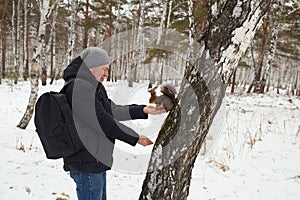 Man feeds squirrel while standing by tree in snowy forest during winter