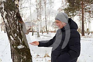 Man feeds squirrel while standing by tree in snowy forest during winter